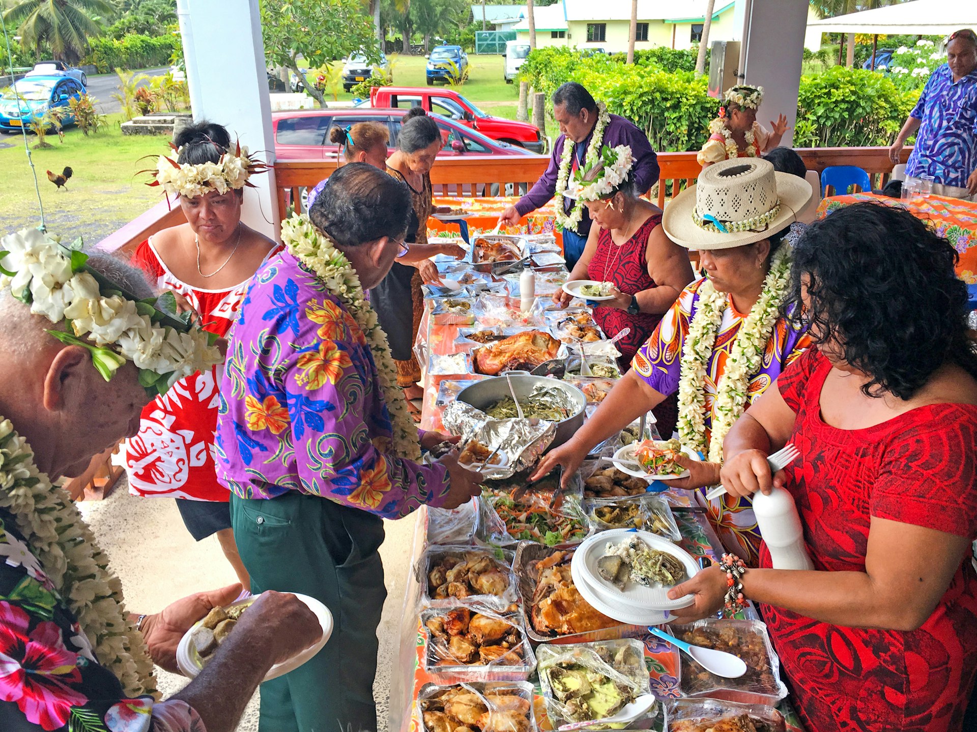 Cook Islanders line up at each side of a long table laden with different dishes during a traditional island celebration