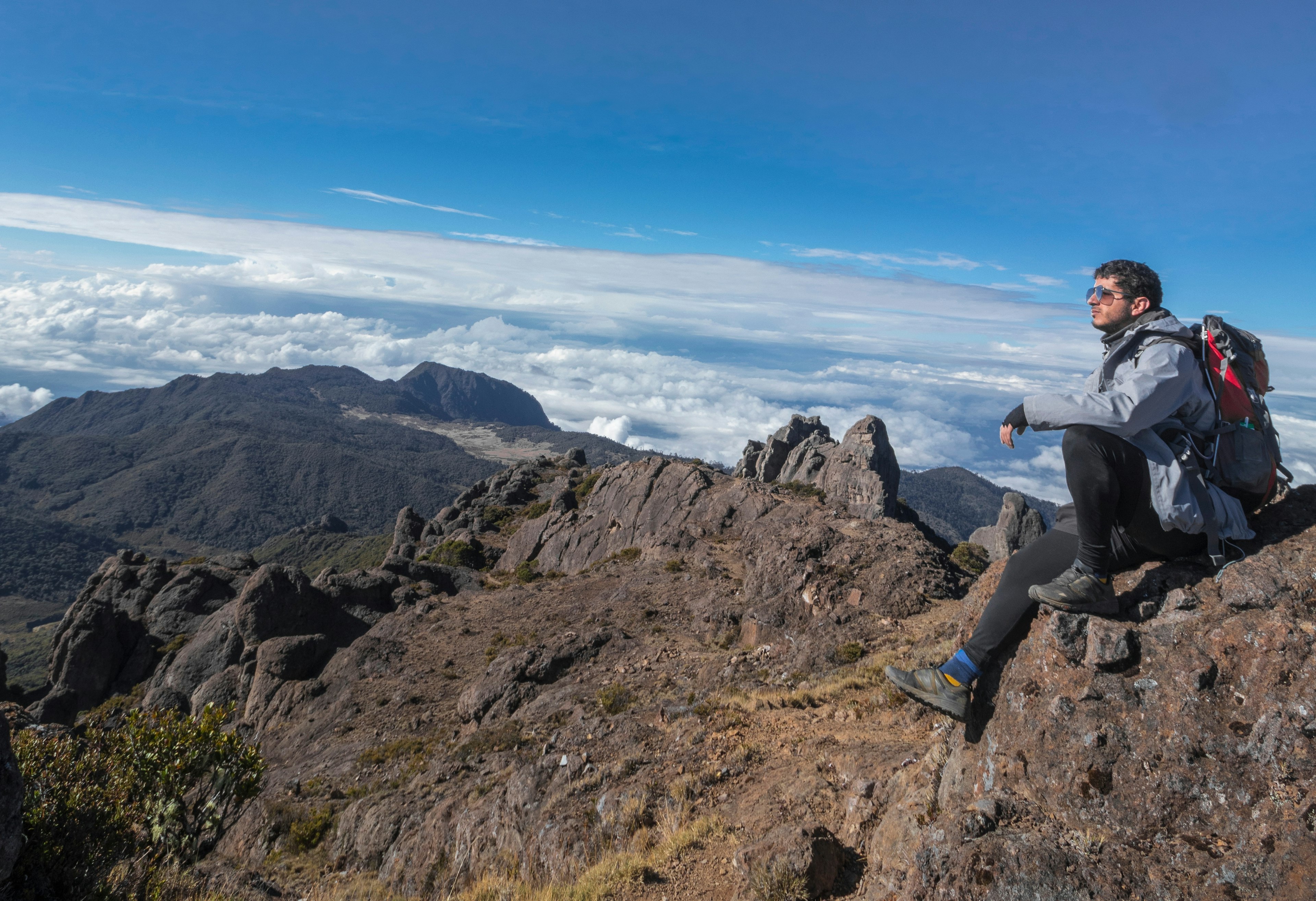 A man sits on a rock looking among peaks and clouds on a sunny morning at Chirripó National Park, Costa Rica, Central America