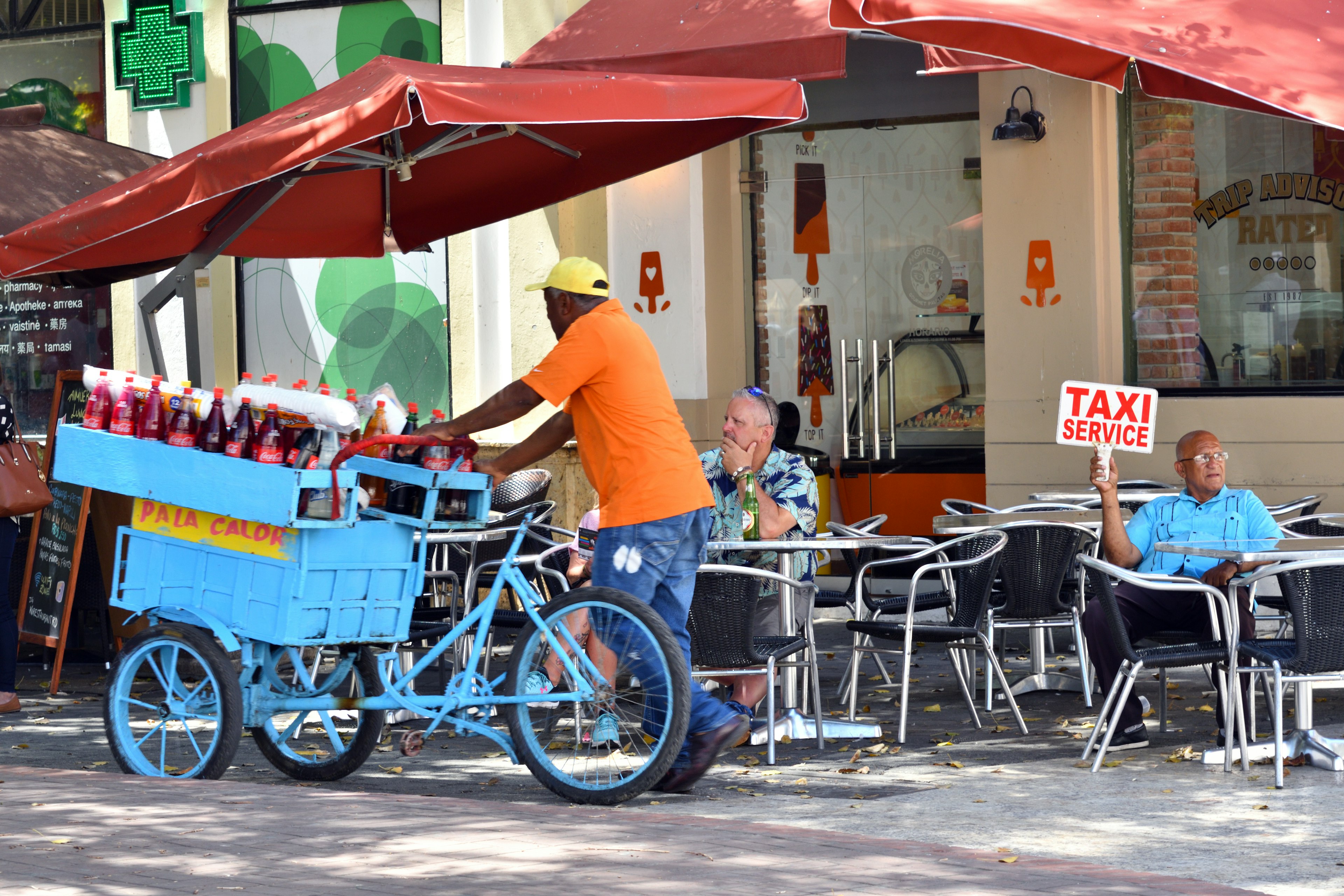 A taxi driver looking for passengers while a drinks cart passes in Santo Domingo, Dominican Republic