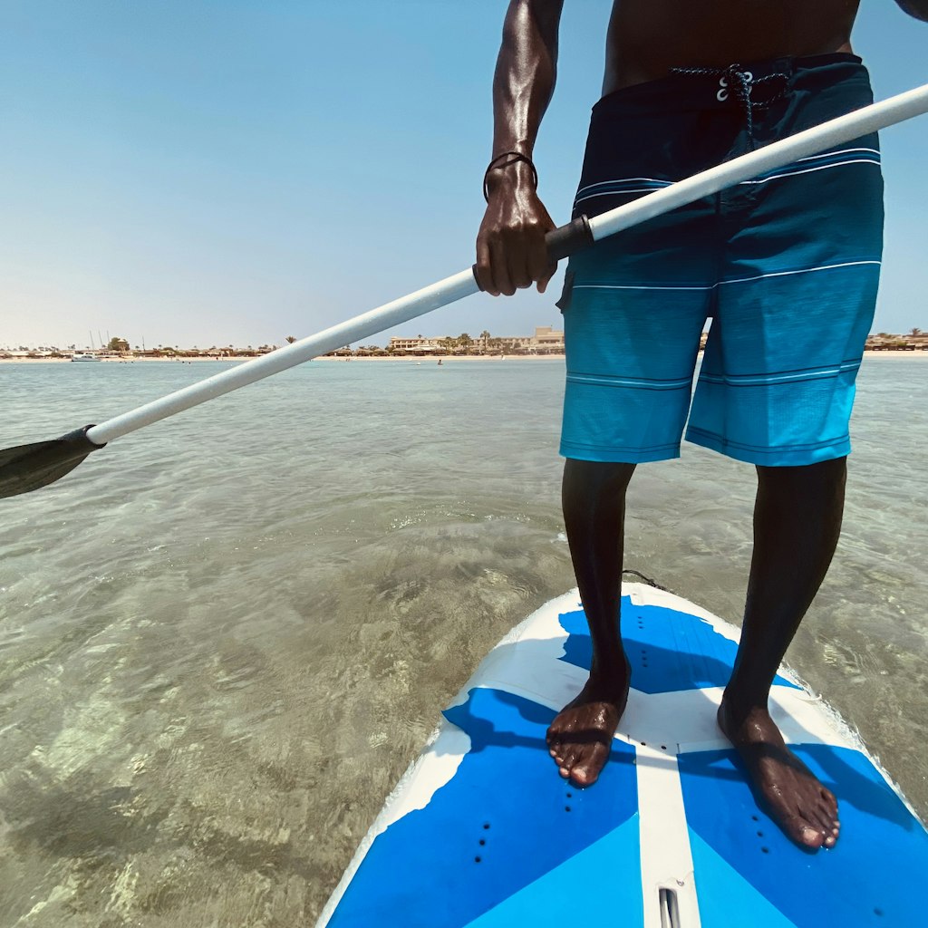 Handsome man surfing on his paddleboard . Active travel concept. Legs standing on paddle board. Close-up.  Beaches are wonderful and the water is calm and crystal clear.