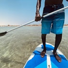 Handsome man surfing on his paddleboard . Active travel concept. Legs standing on paddle board. Close-up.  Beaches are wonderful and the water is calm and crystal clear.