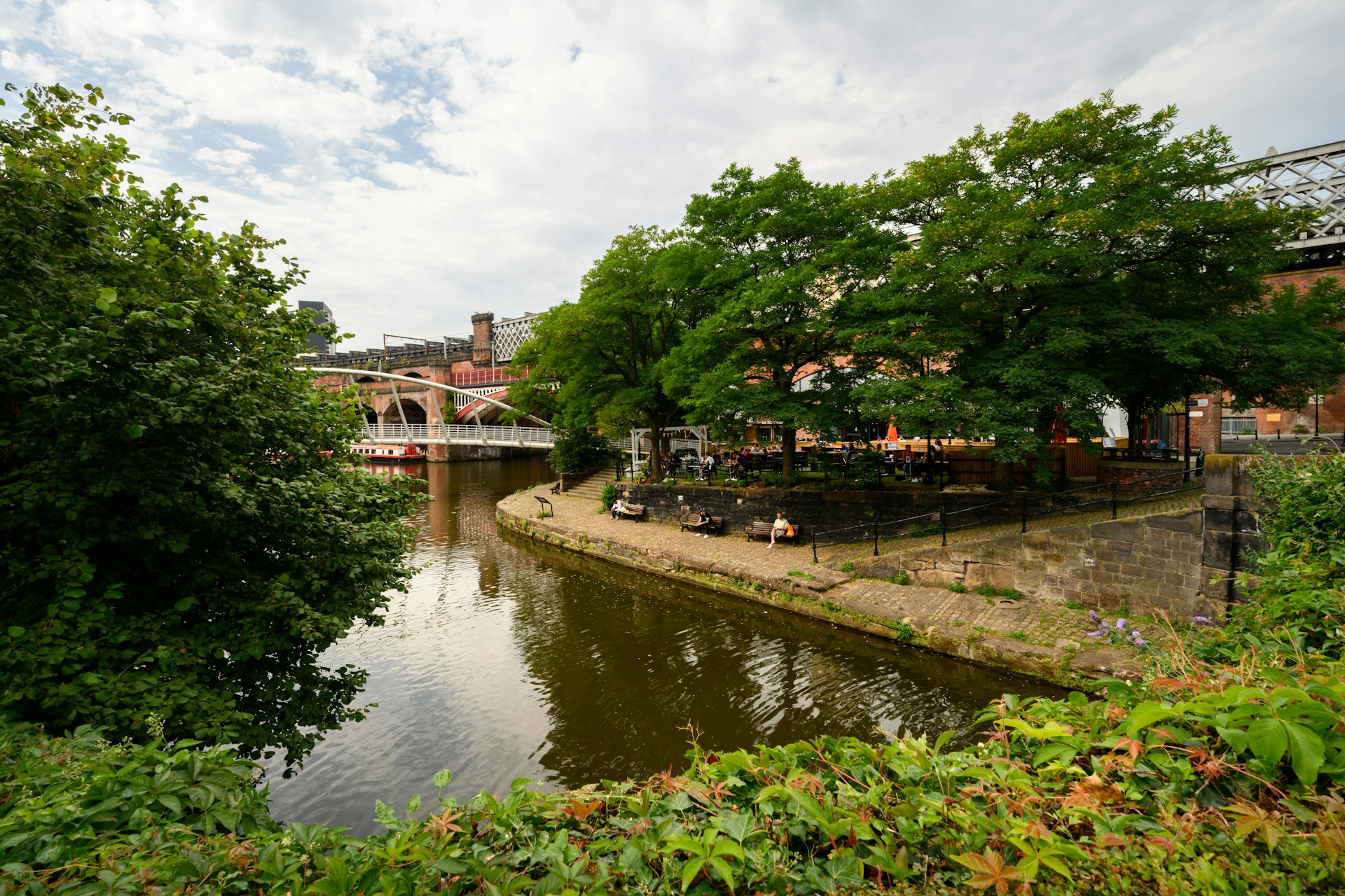 People sitting on benches lining a waterway in Castlefield, Manchester, England