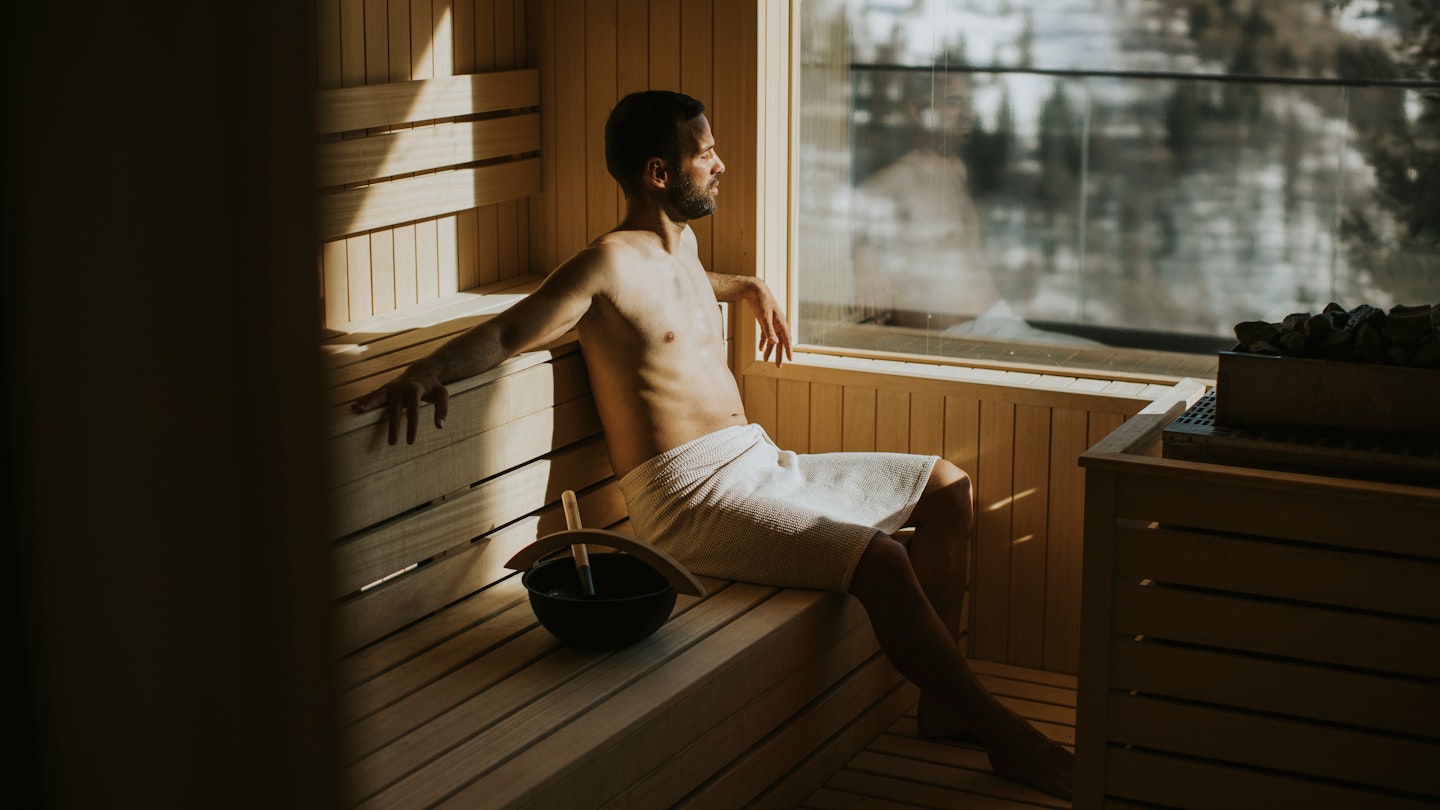 Handsome young man relaxing in the sauna and watching winter forest through the window