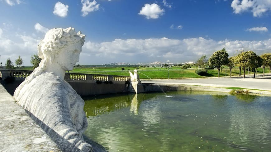 A statue in a fountain at Parc Borély, with the Marseille skyline seen beyond a green lawn, Marseille, Bouches-du-Rhône, France