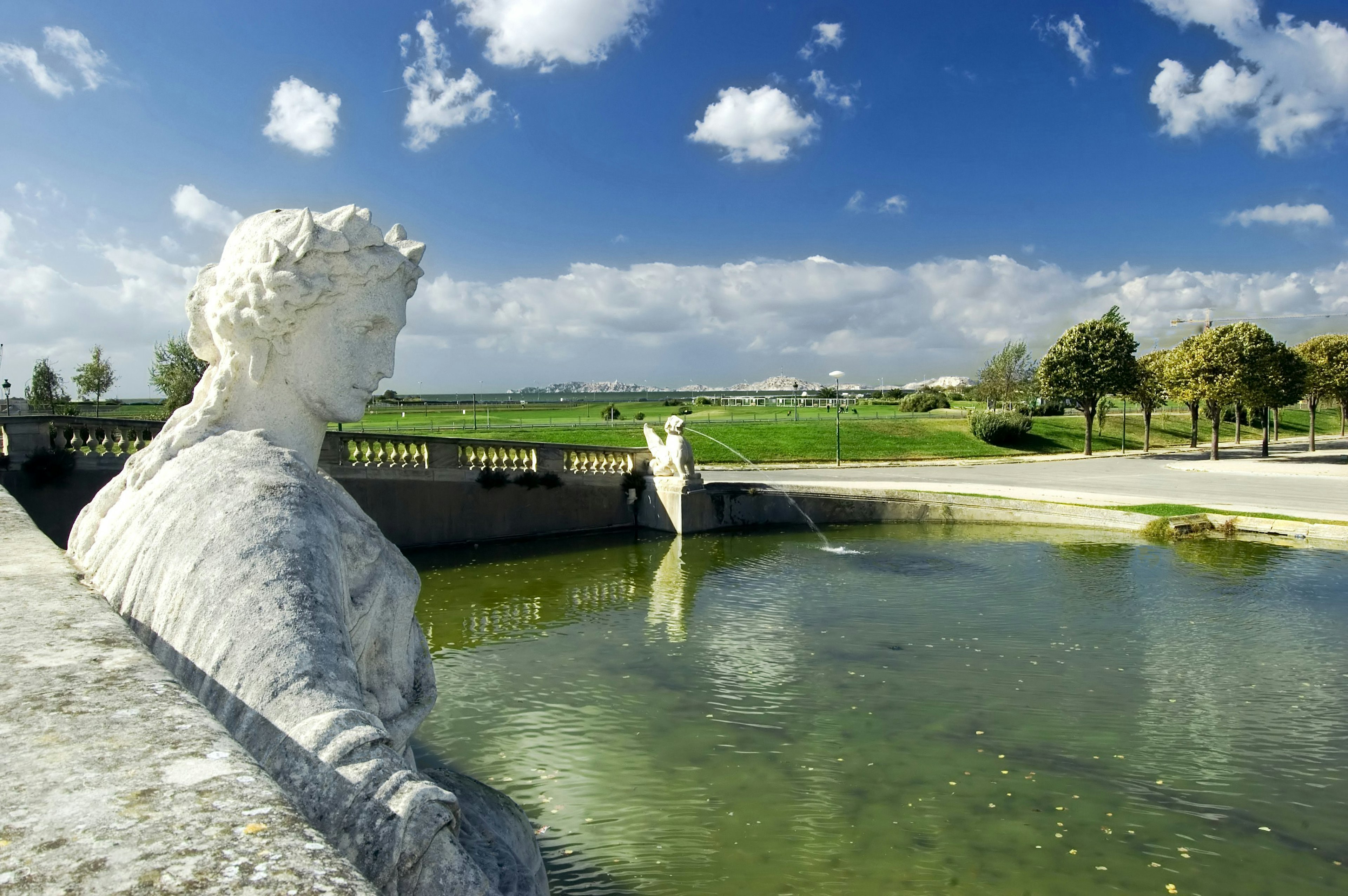 A statue in a fountain at Parc Borély, with the Marseille skyline seen beyond a green lawn, Marseille, Bouches-du-Rhône, France