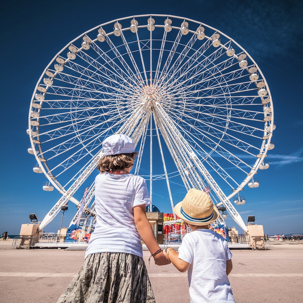 Children holding hands in front of a ferris wheel. Childhood, Poetry, Fisheye, Marseille, Provence, France