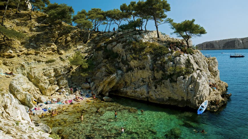 A small cove at the foot of rocky sea cliffs with people sunbathing and playing in the water