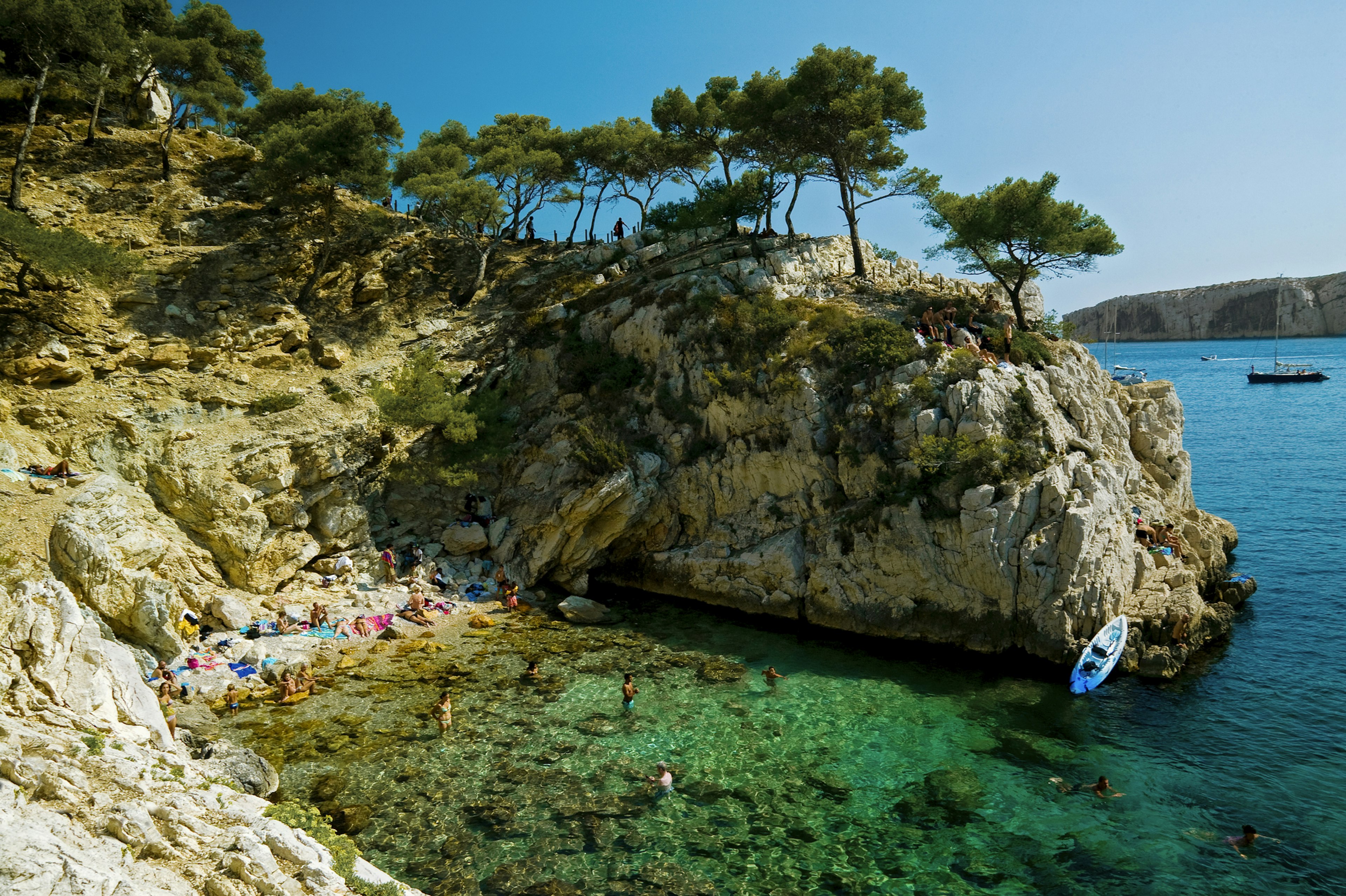 A small cove at the foot of rocky sea cliffs with people sunbathing and playing in the water