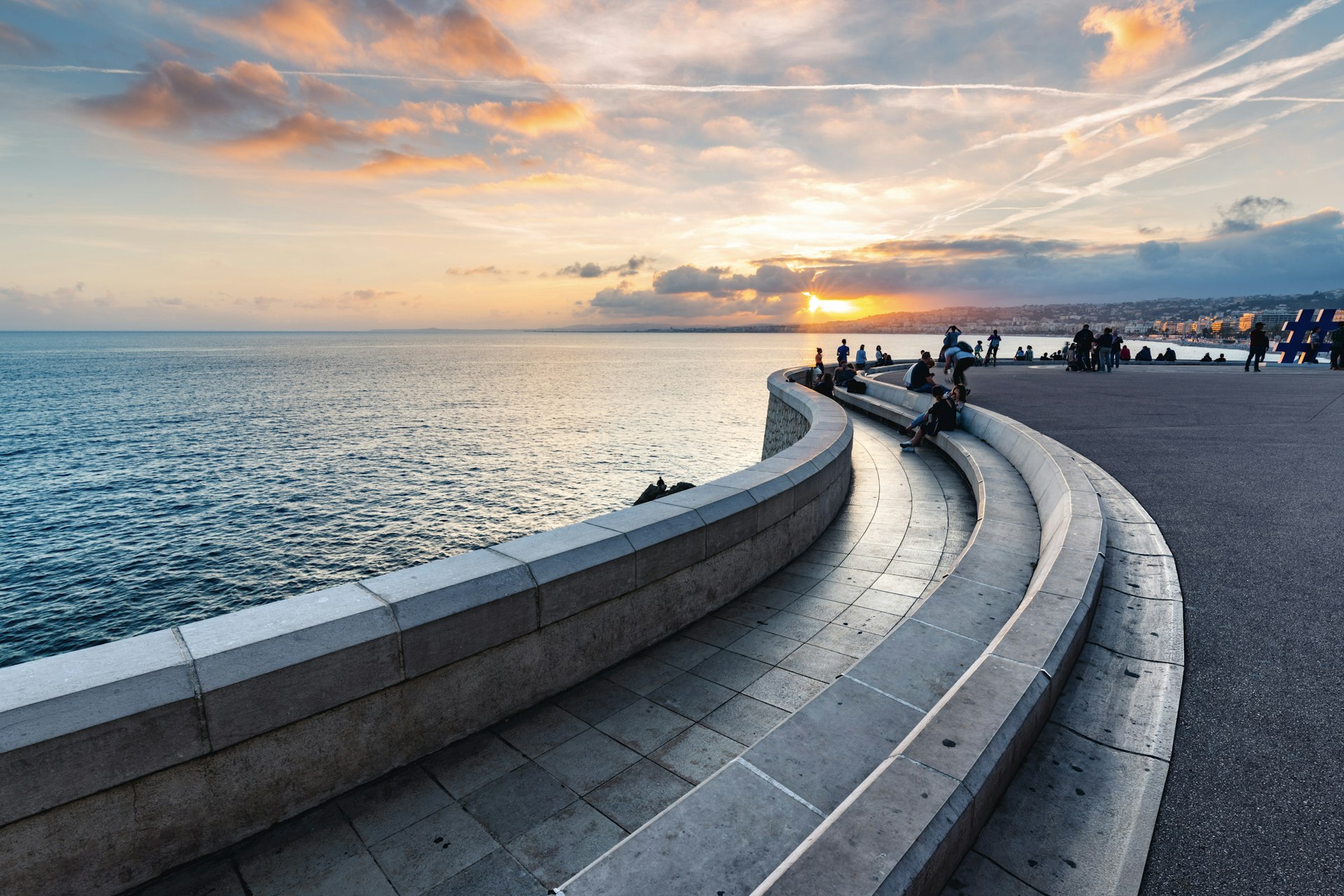 A waterfront promenade at sunset, Nice, France, with people in silhouette as the sun sets in the distance