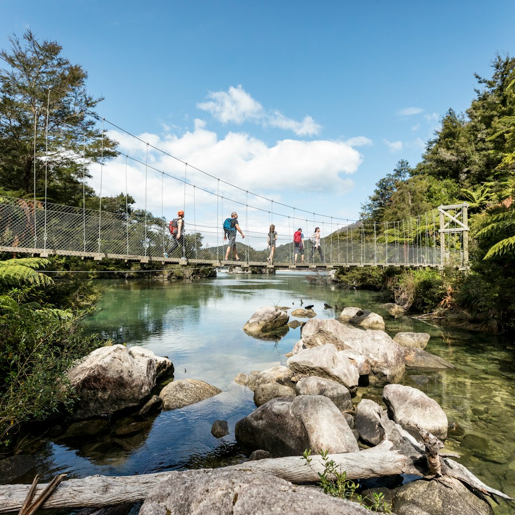 Family of five walking a rope suspension bridge across a calm lagoon