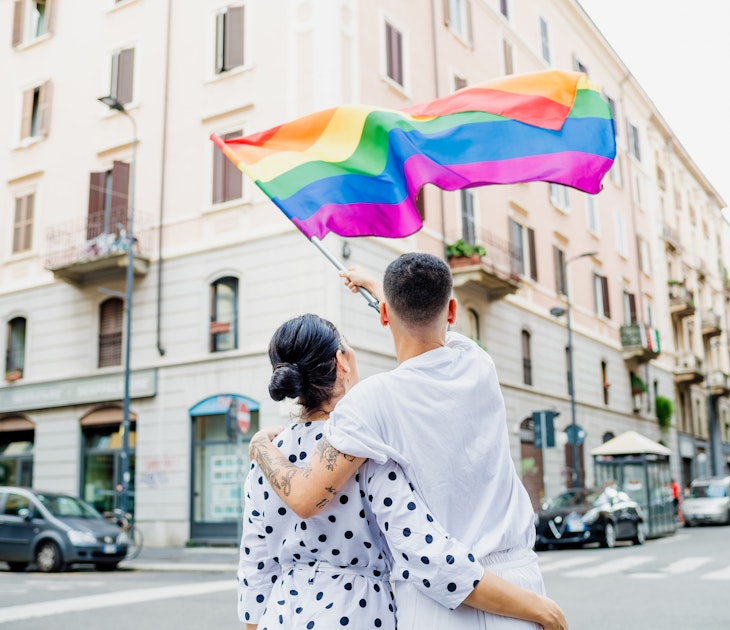 Rearview of young lesbian couple standing on a street, waving a rainbow flag
