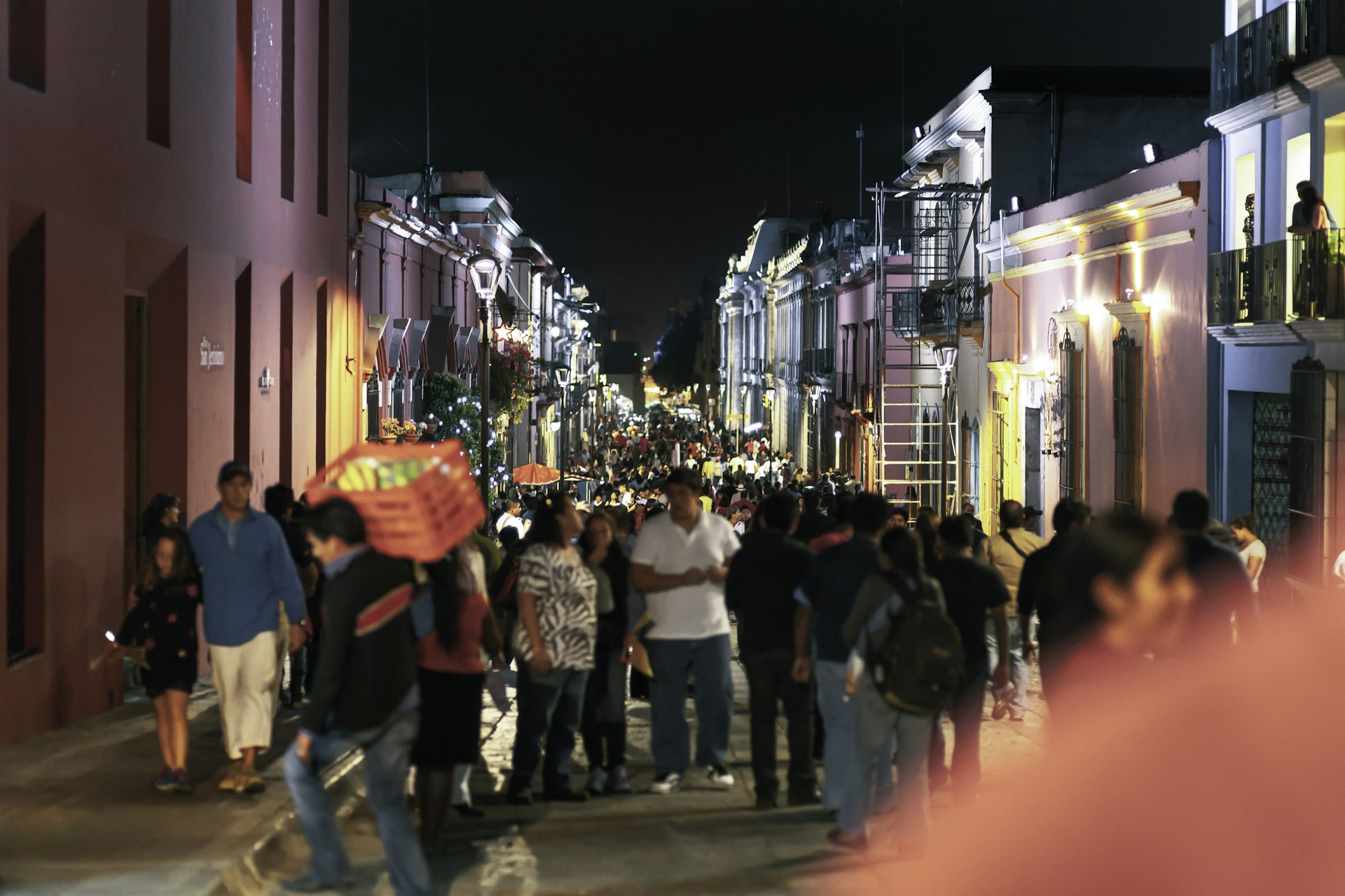 We see a crowded night street in downtown Oaxaca City in Mexico, during the celebration time and annual Guelaguetza celebration. the street is very crowded; the focus is in the background; the front people are in soft focus.
