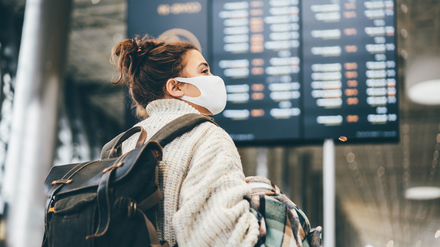 Woman in protection mask looking at information in airport.