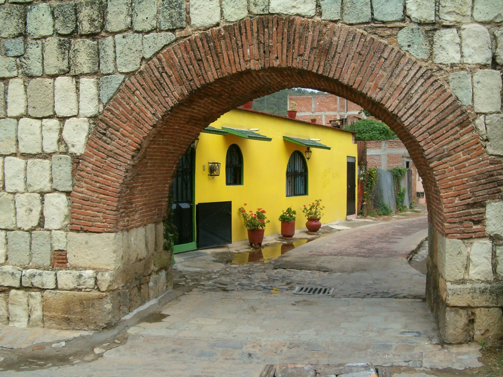 Yellow house behind an arch in the Xochimilco Aqueduct in Oaxaca City, Mexico. The wall was built of Oaxaca's typical volcanic green stone.