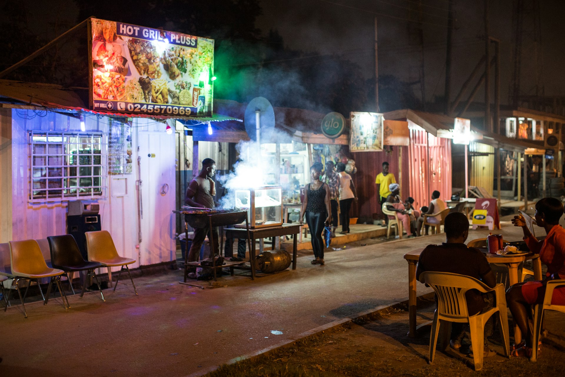 People enjoy food and drinks at roadside bars and restaurants on a car-free street at night in Accra, Ghana, West Africa