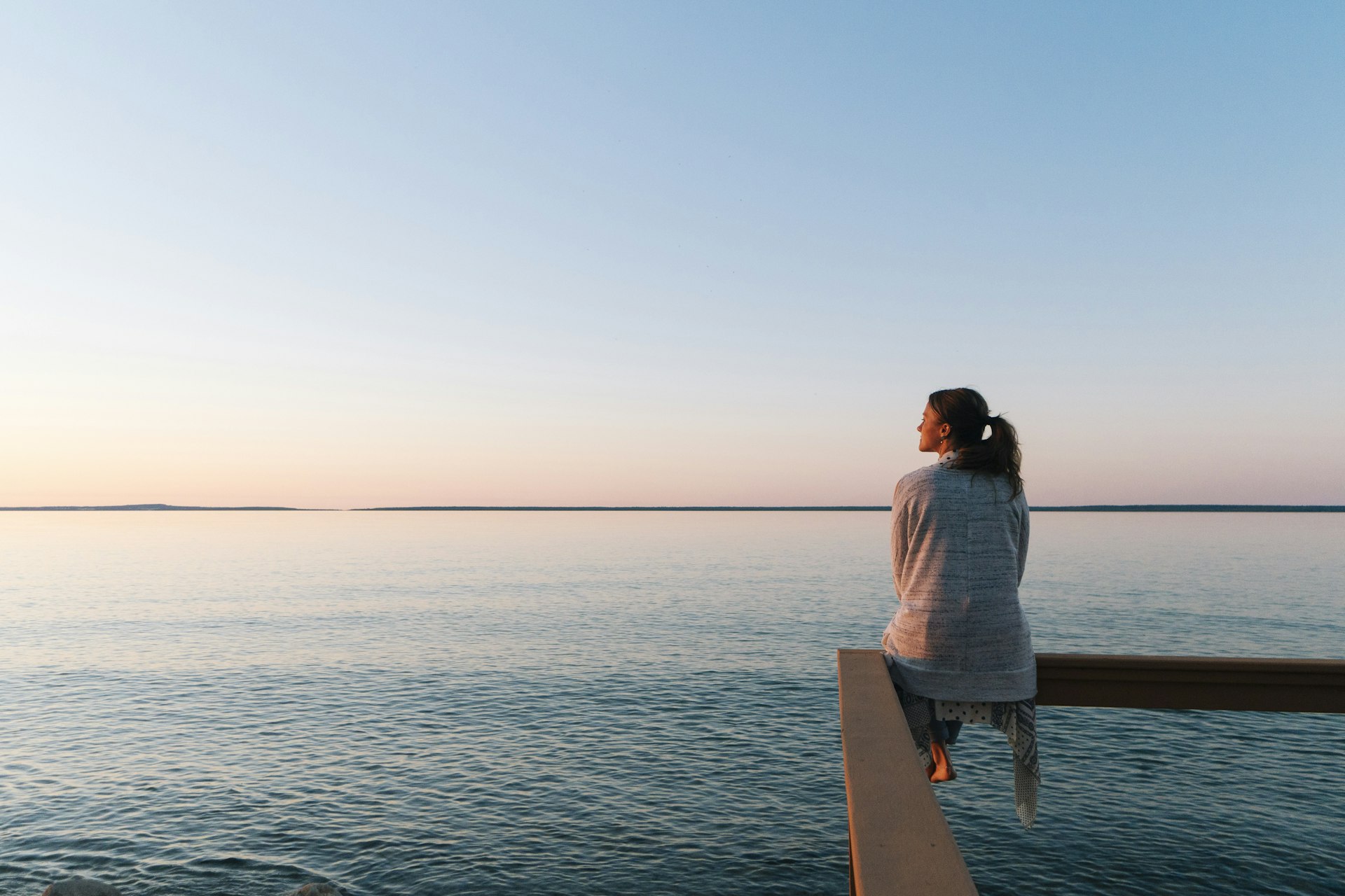 Young woman sitting on edge looks out at view of a lake