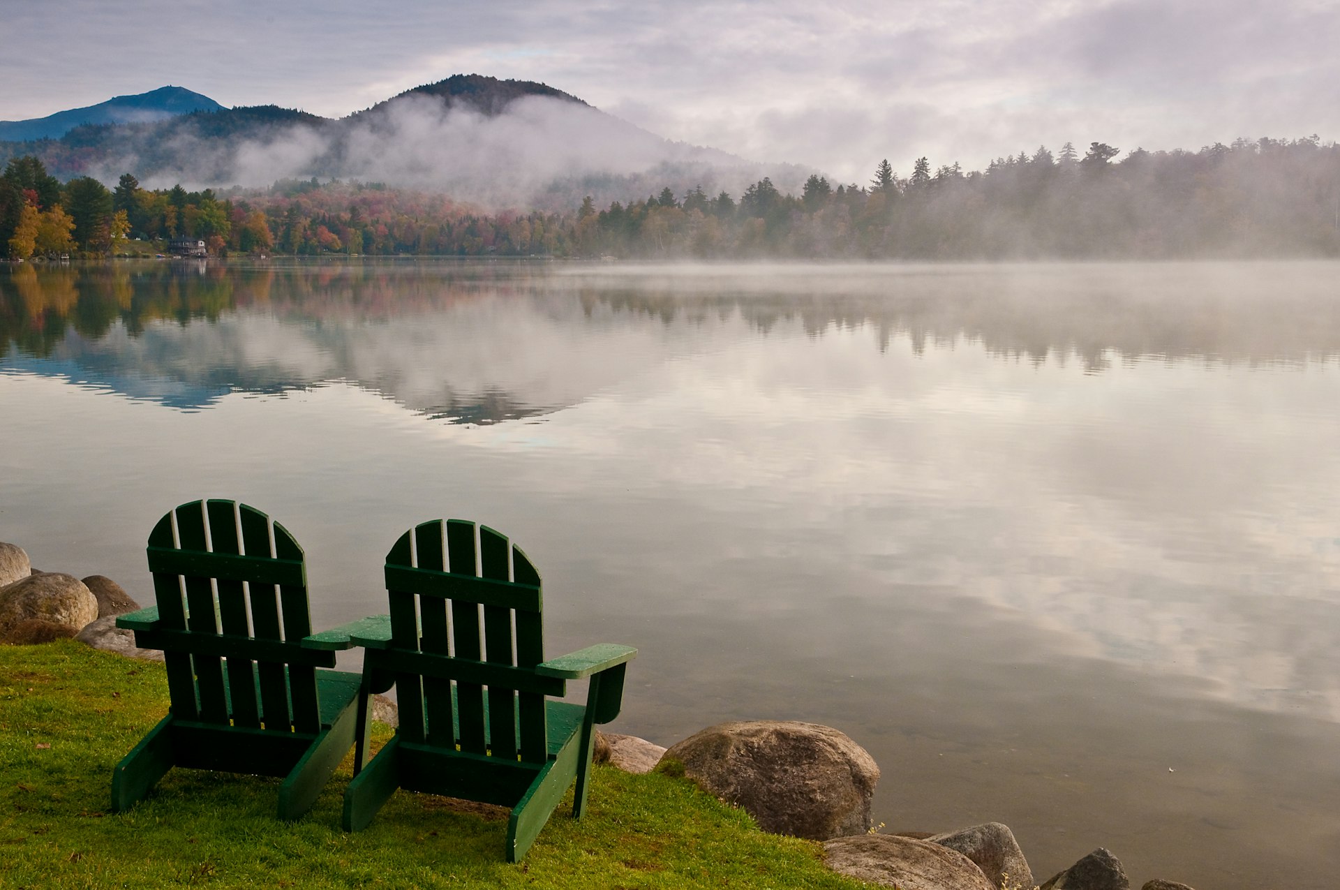 Empty wooden chairs by lake with mountain reflection at Lake Placid, NY