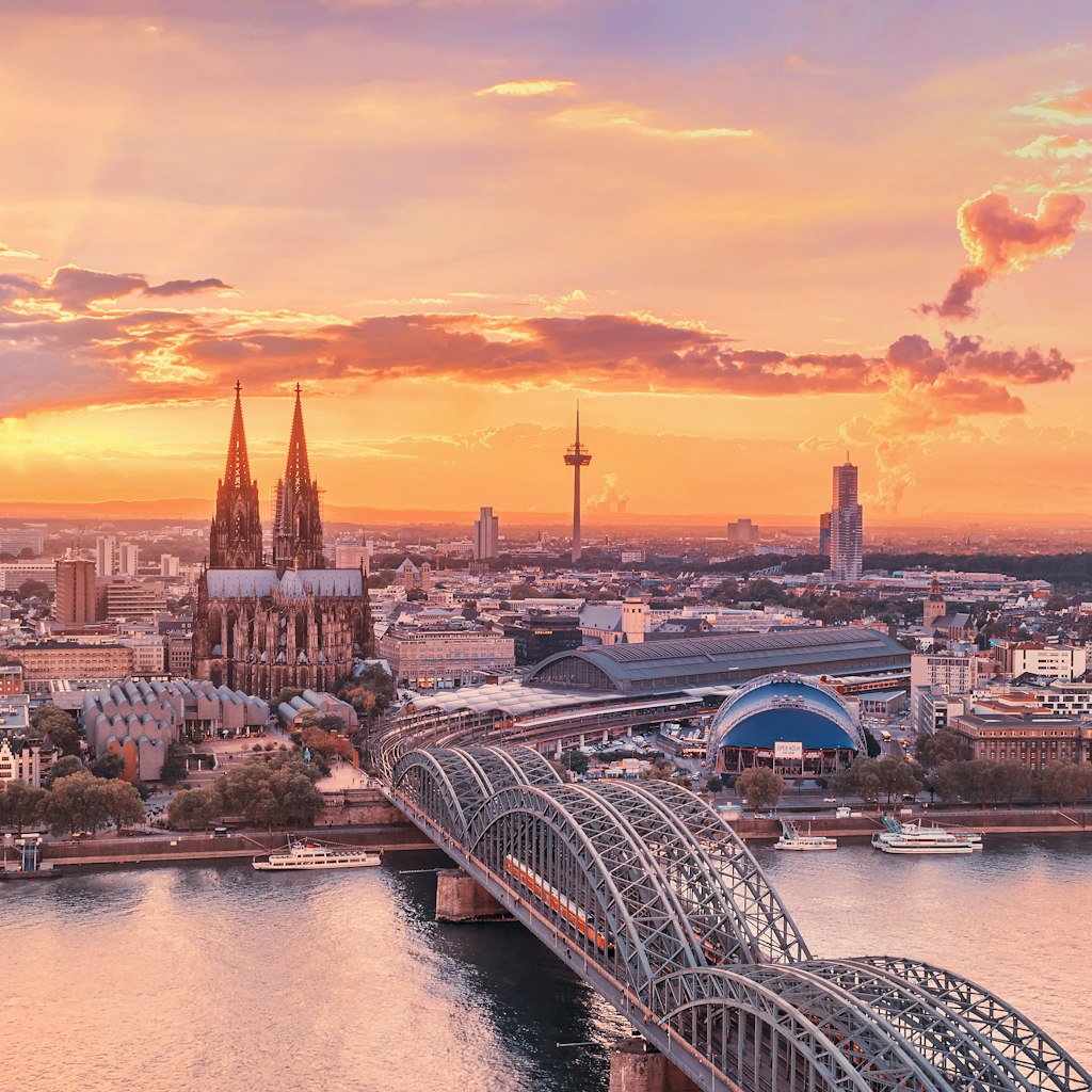 The Cathedral (Dom), TV Tower (Clonius), the Musical Dome, Kölner Philharmonie, the river Rhine, Hohenzollern Bridge, Museum Ludwig and Old Town are featured beyond a colourful sky.