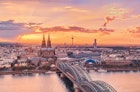 The Cathedral (Dom), TV Tower (Clonius), the Musical Dome, Kölner Philharmonie, the river Rhine, Hohenzollern Bridge, Museum Ludwig and Old Town are featured beyond a colourful sky.