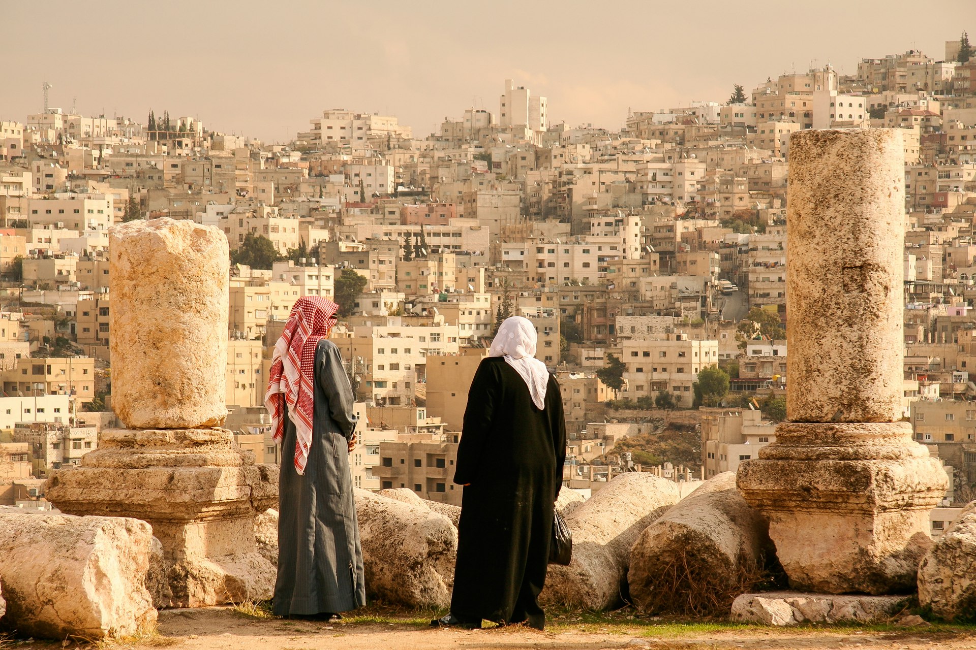 Two people in traditional Jordanian dress look out over the heavily developed hillsides of Amman