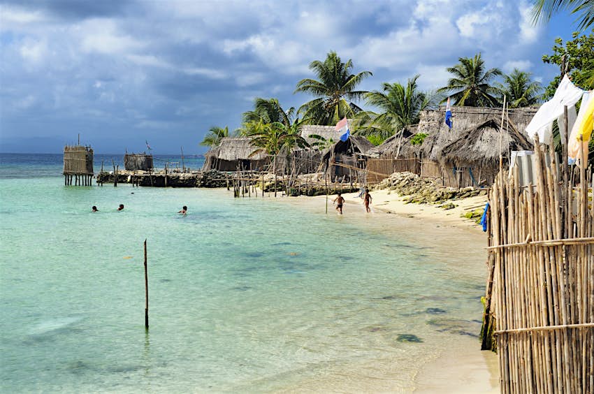 Blue waters lap a beach with thatched-roof buildings in Nalunega, San Blas Islands, Panama 