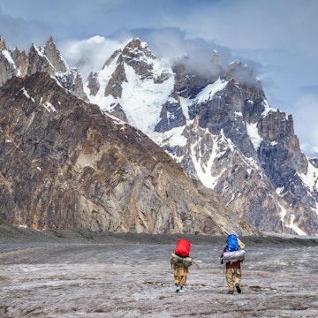Two Balti porters walking on Biafo glacier, with Karakoram mountains in background, during Biafo Hispar Snow Lake trek between Baintha and Marphogoro, in Central Karakoram National Park.