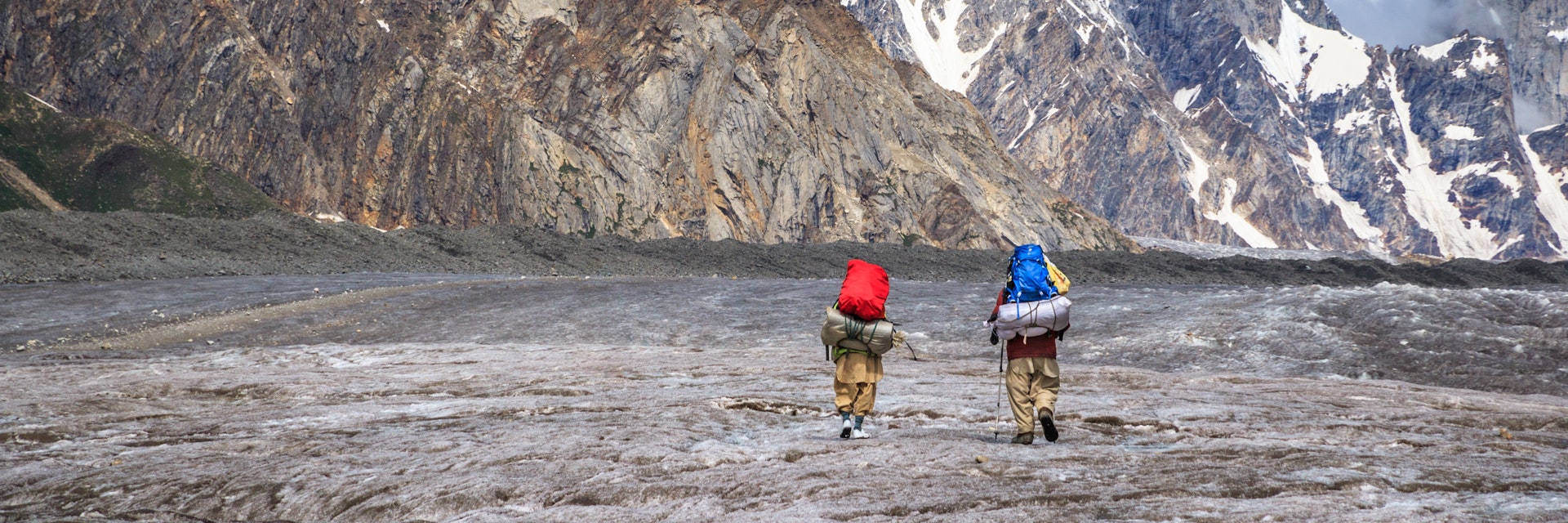Two Balti porters walking on Biafo glacier, with Karakoram mountains in background, during Biafo Hispar Snow Lake trek between Baintha and Marphogoro, in Central Karakoram National Park.