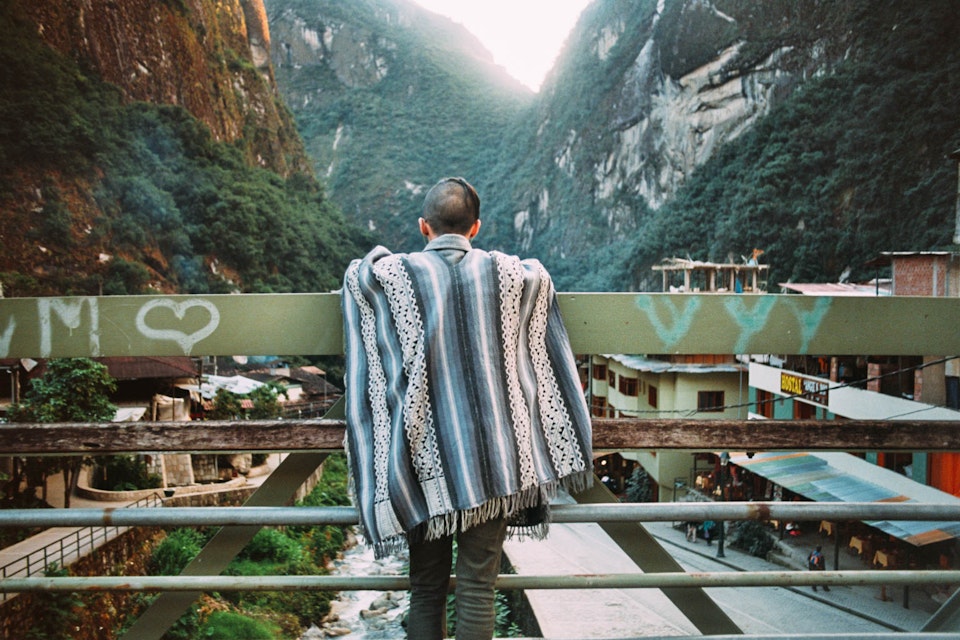 A man wearing a Peruvian poncho leaning on the rails of a bridge at Aguas Calientes.