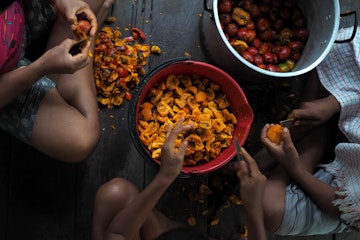 Children skinning fruits on the floor of a kitchen in Leticia.