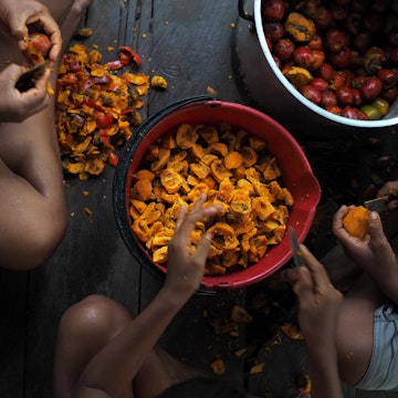 Children skinning fruits on the floor of a kitchen in Leticia.