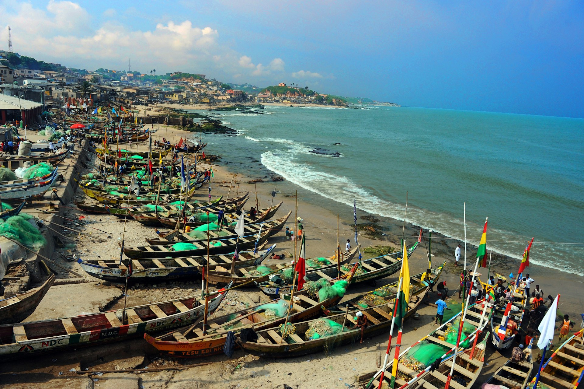 Wooden fishing boats with colorful flags dominate a sandy beach