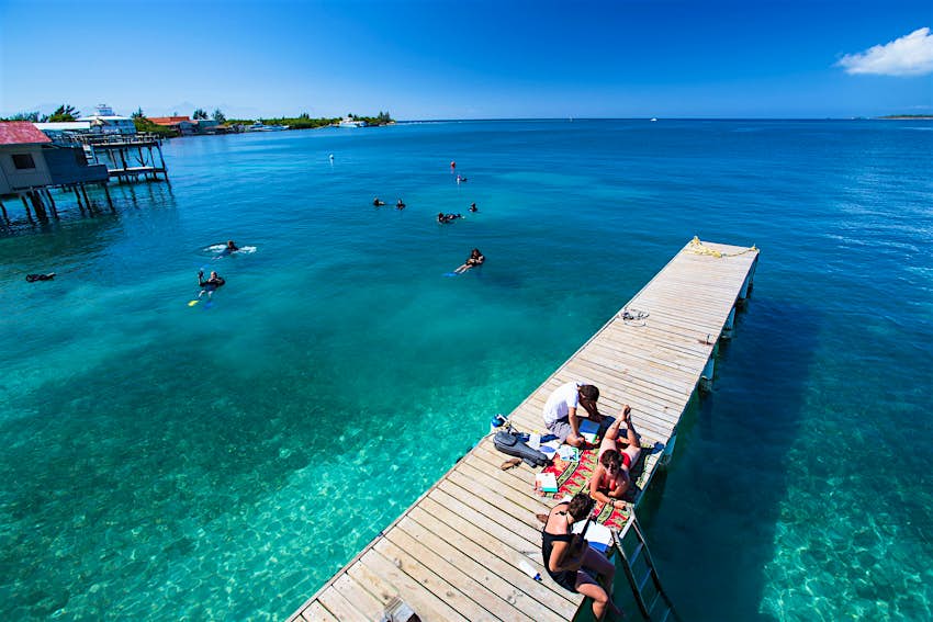 Girls play music in the sun on a Utila dock with snorkelers in the blue-green water behind them