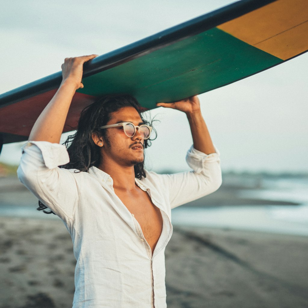 An Indonesian man holding a surfboard on a beach in Bali