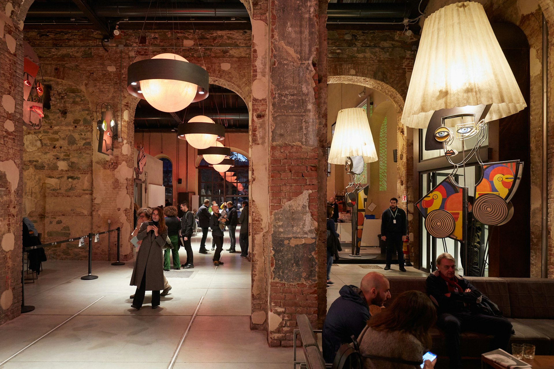 The interior of Officine Grandi Riparazioni with people moving around looking at displays of modern art