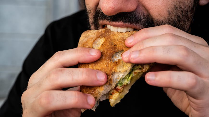 Un homme barbu mange un sandwich grillé à Turin, Italie