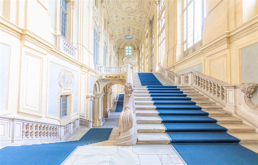 A vast white marble staircase with blue carpets running up the middle 