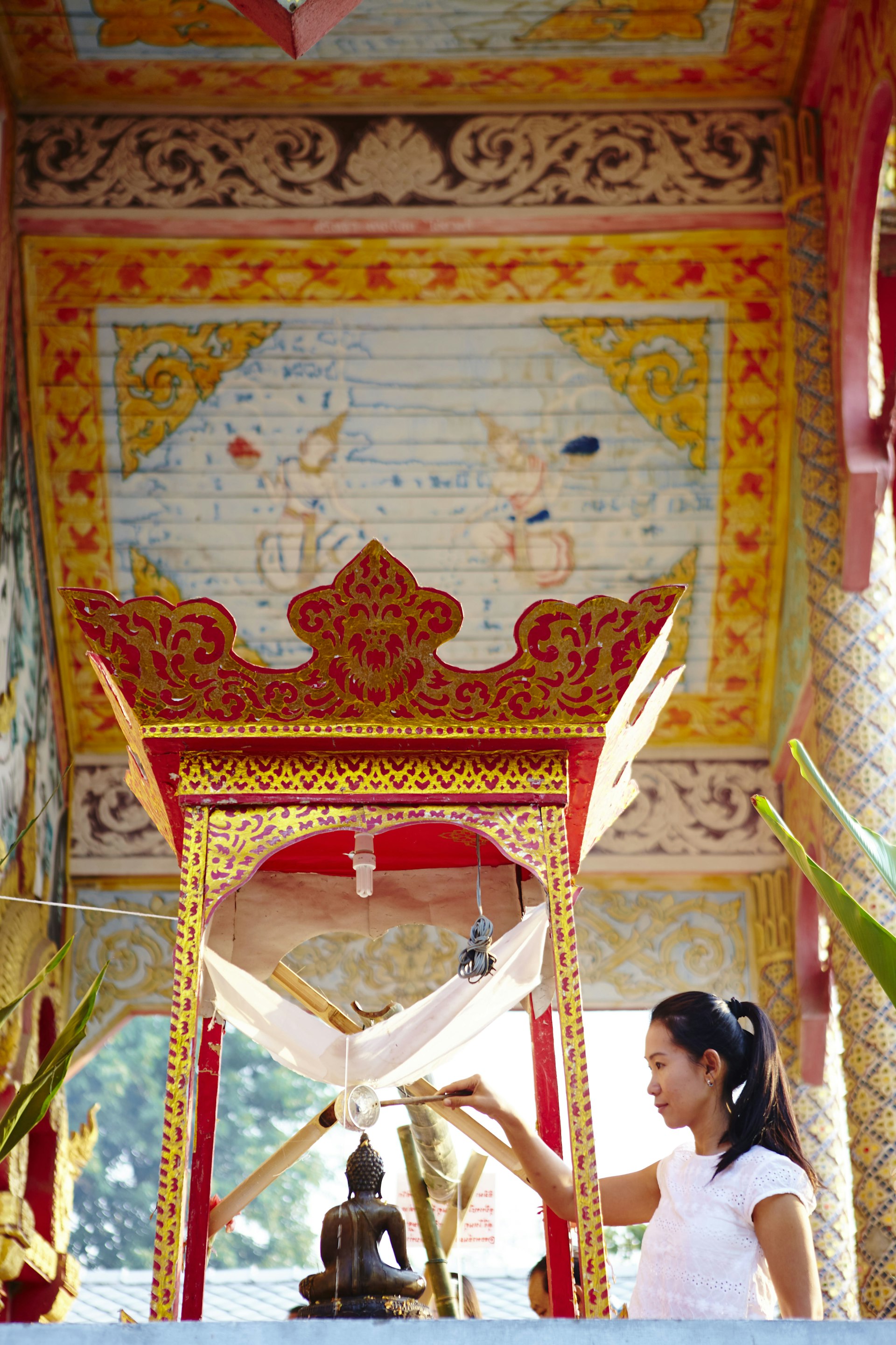 Woman pouring water over Buddha, cleansing sins and bad luck during Songkran Festival.