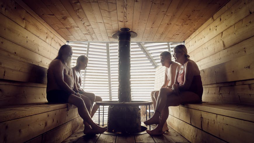 Four people are silhouetted in a wooden sauna room with a central stove in Helsinki, Finland