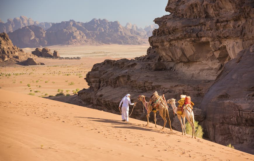 A Bedouin guide leads his two dromedary camels over the tall dunes of Wadi Rum, Jordan, Middle East