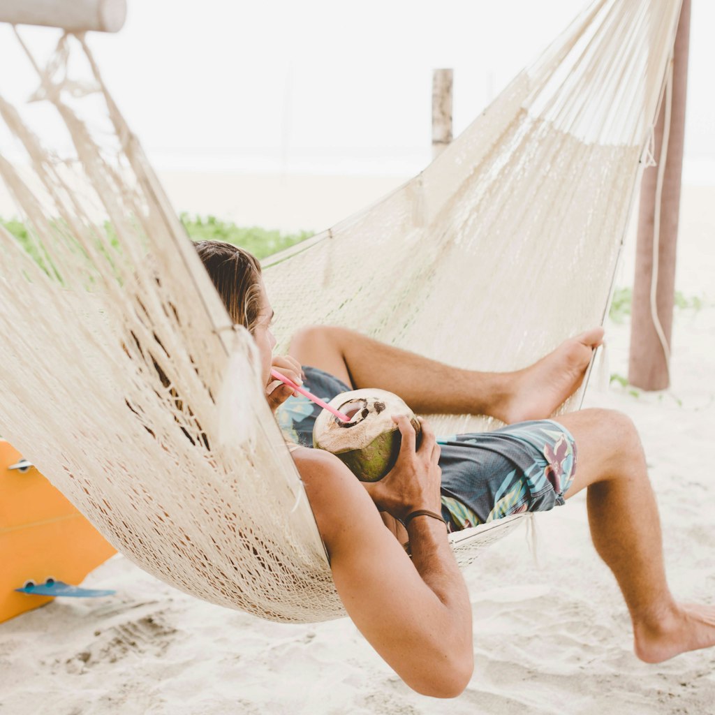 Man enjoying coconut water in hammock on beach