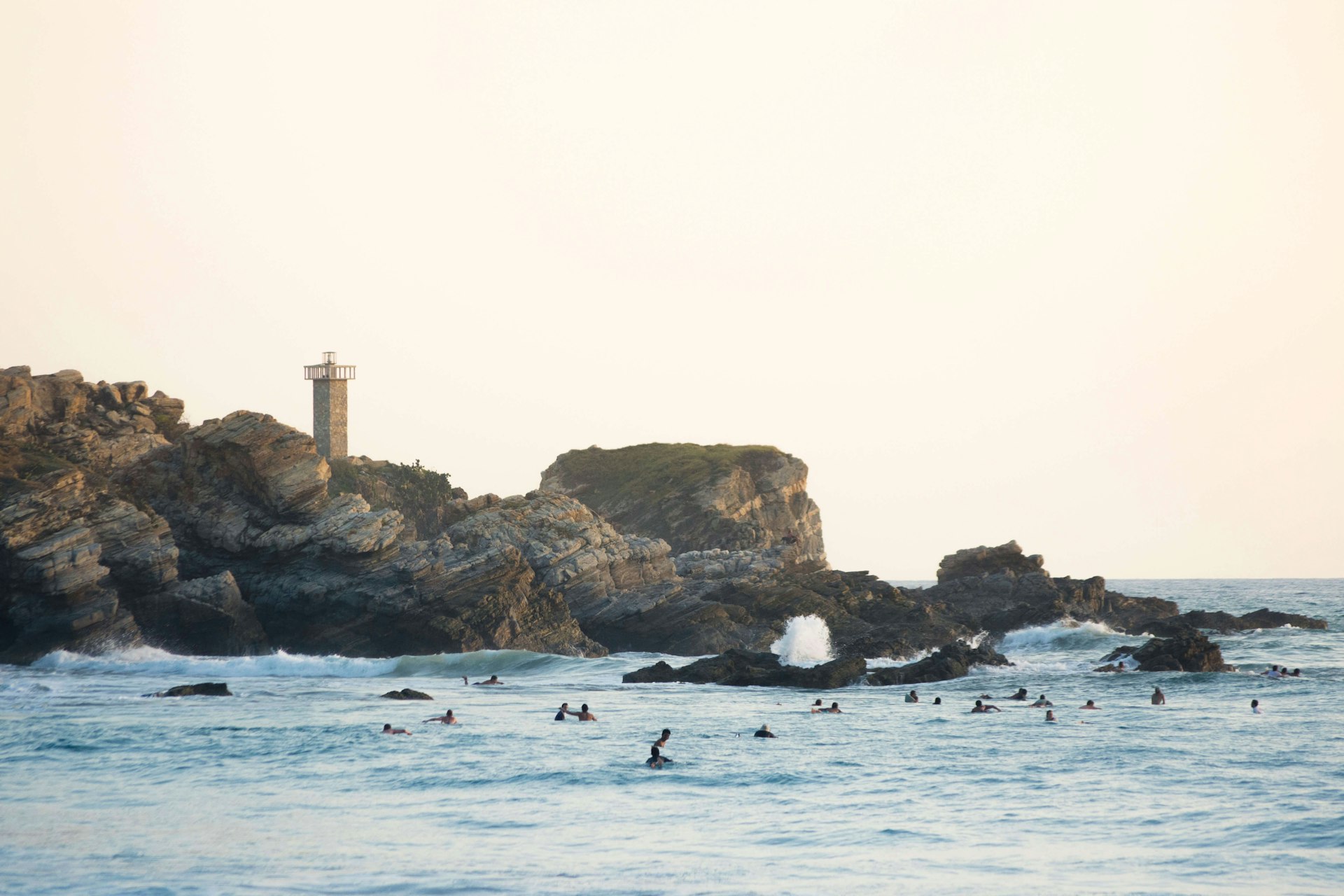 Evening light paints the lighthouse of Punta Zicatela, while many surfers pack the lineup in Puerto Escondido, Mexico