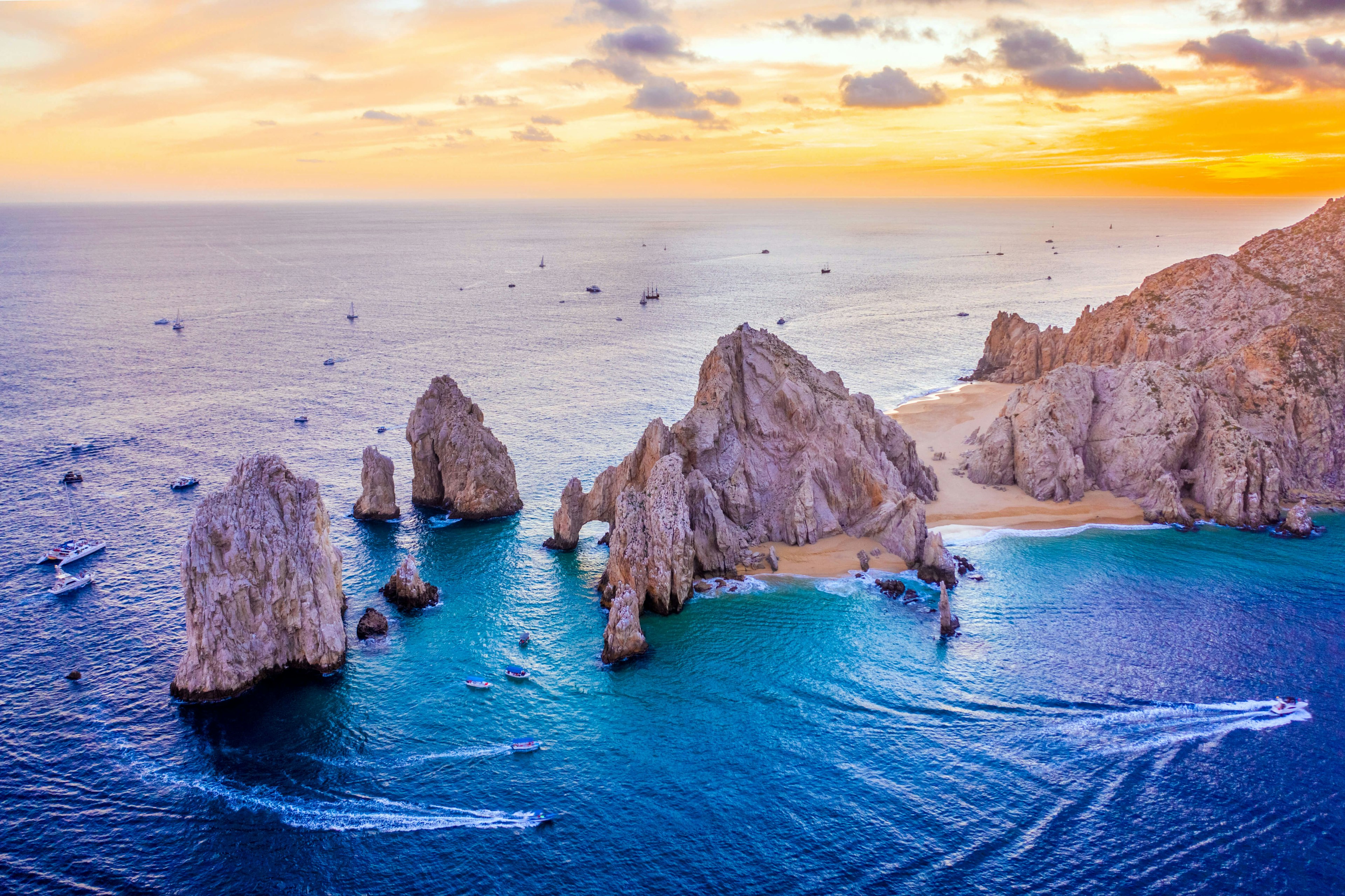 Aerial view of boats speeding by El Arco de Cabo San Lucas, Mexico at sunset