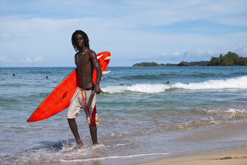 Bocas Del Toro, Panama - October 18, 2008: A Panamanian surfer with dread locks walks with his surfboard at Wizard Beach, located on Isla Bastimentos in the Bocas del Toro Archipelago. He is giving the hang loose sign with his left hand.
