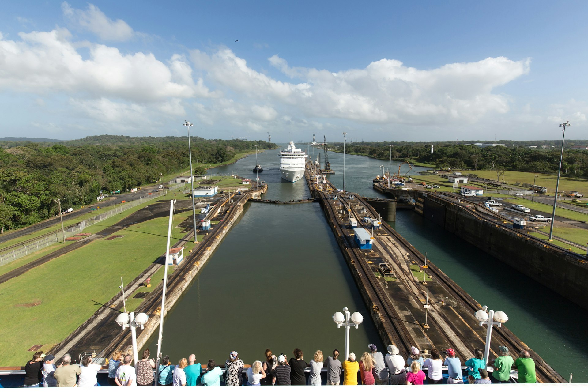 A line of people gaze at an approaching cruise ship in a narrow waterway at Panama Canal