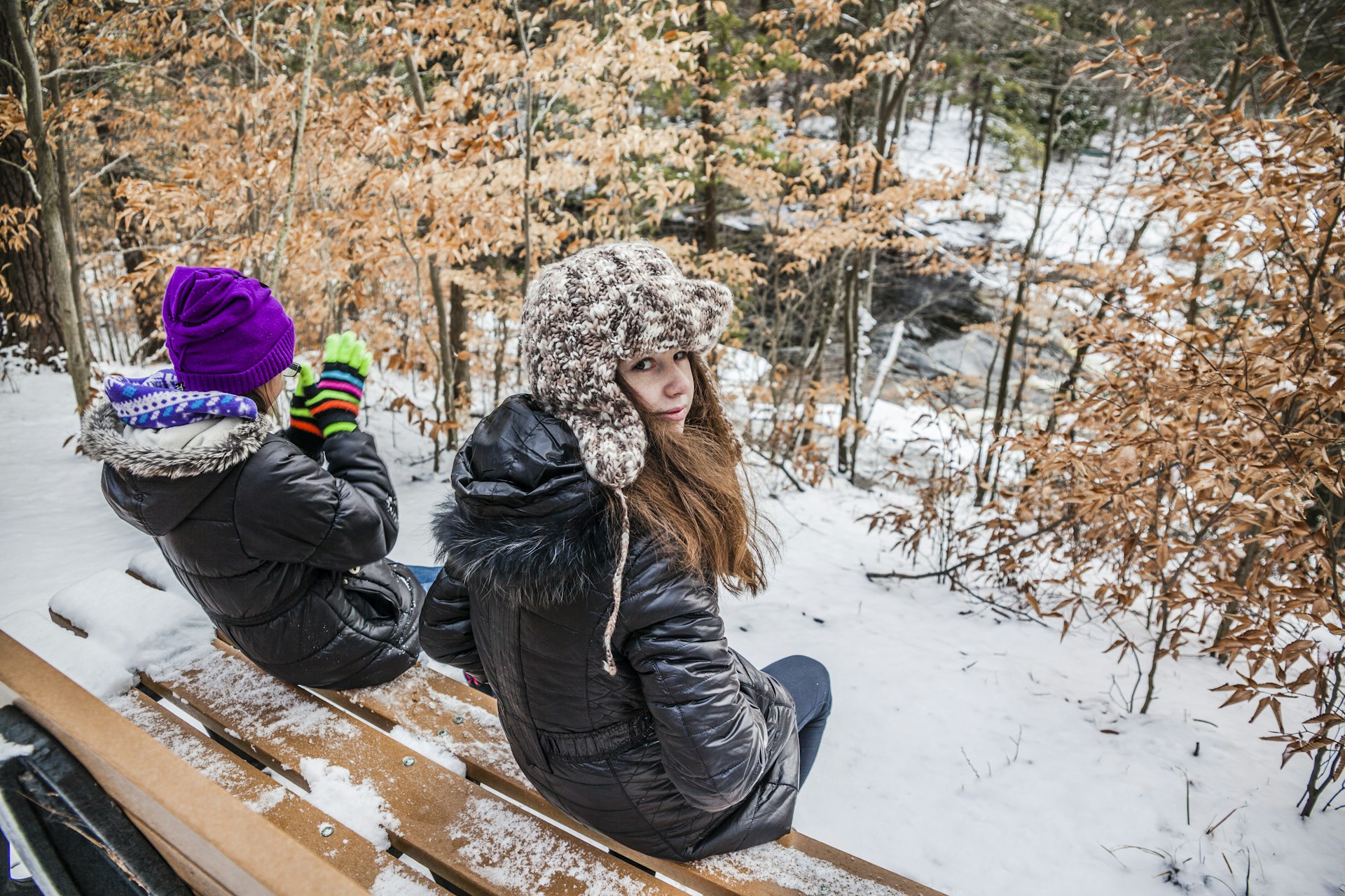 Two girls sits at the bench in the winter forest. Pennsylvania, Poconos, Austin T. Blakeslee natural are