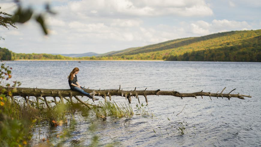 Teenager girl walking on the falled tree over the Mauch Chunk lake. The sunny autumn's day in Poconos, Pennsylvania, USA