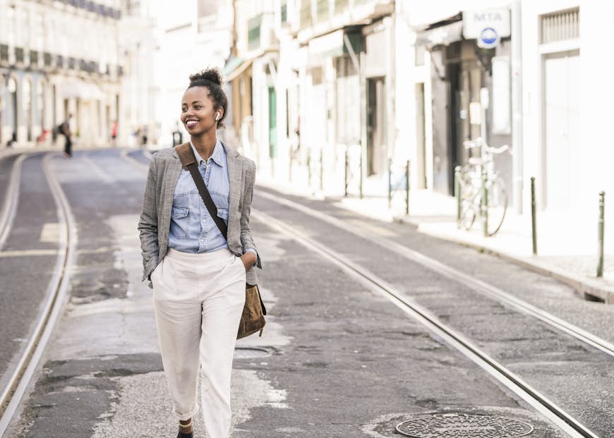 Smiling young woman with wireless earphones in the city on the go, Lisbon, Portugal