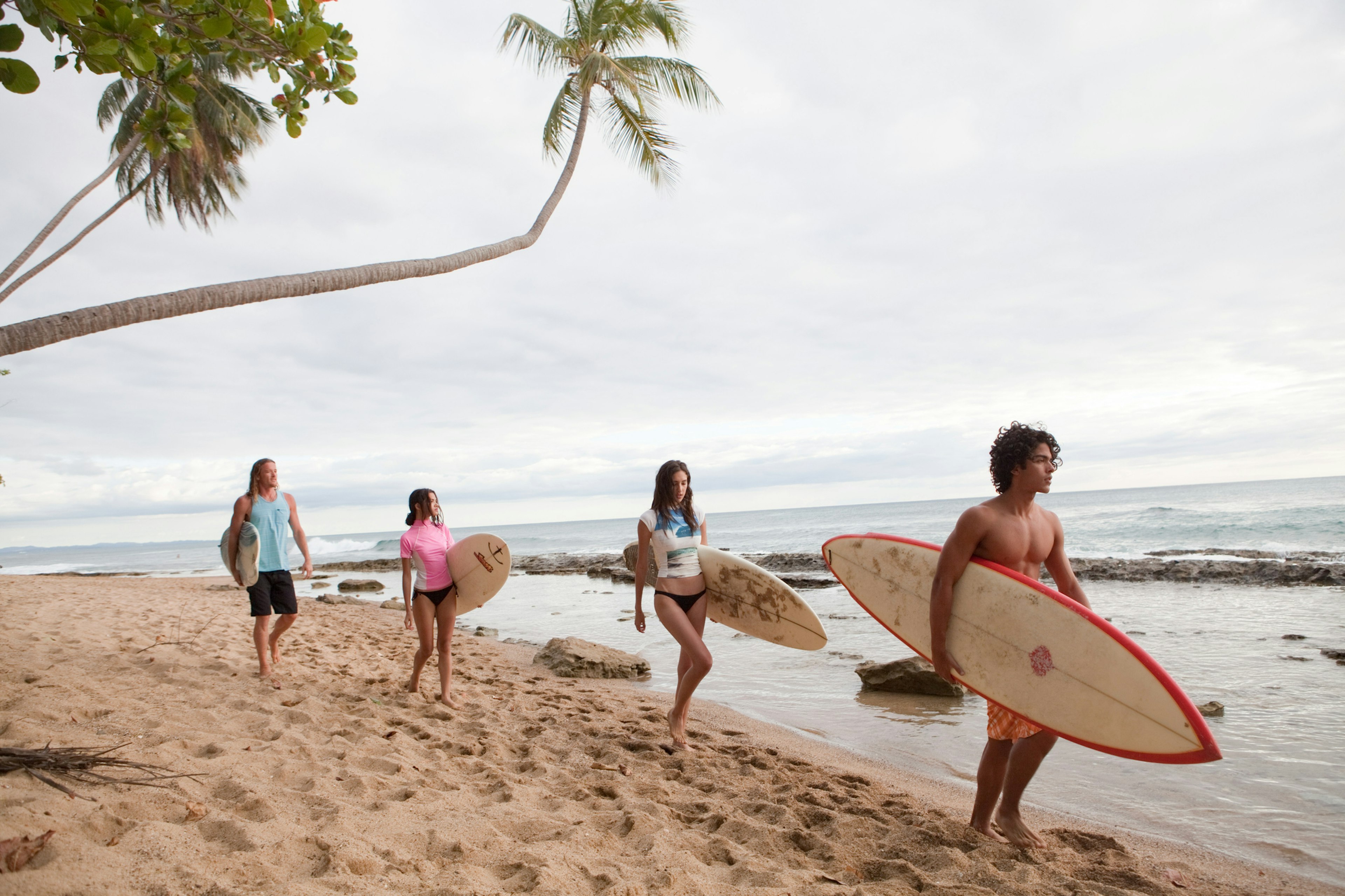 Four young friends carrying surfboards on beach