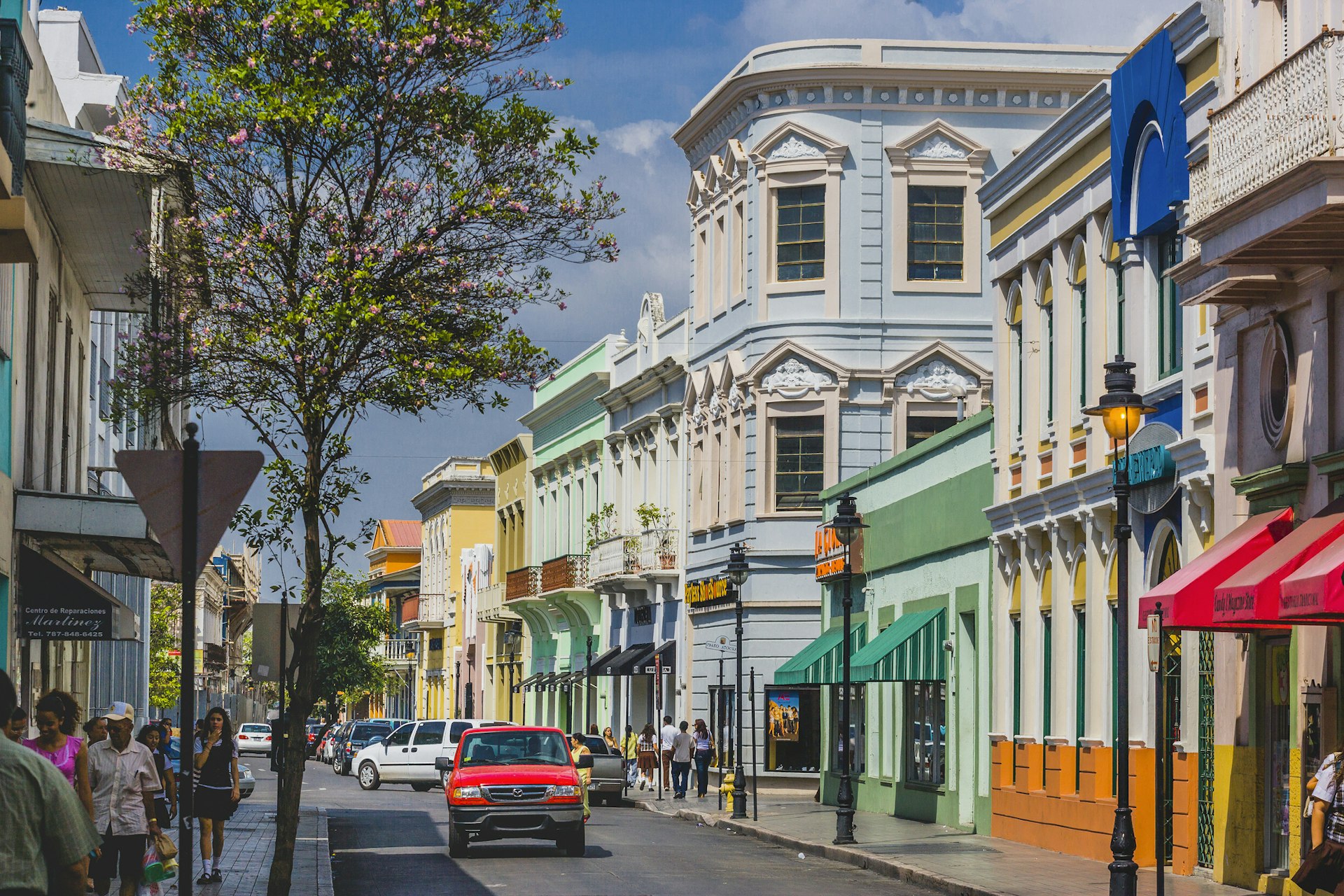 A red car drives down a street lined with pastel-colored buildings in the city of Ponce, Puerto Rico