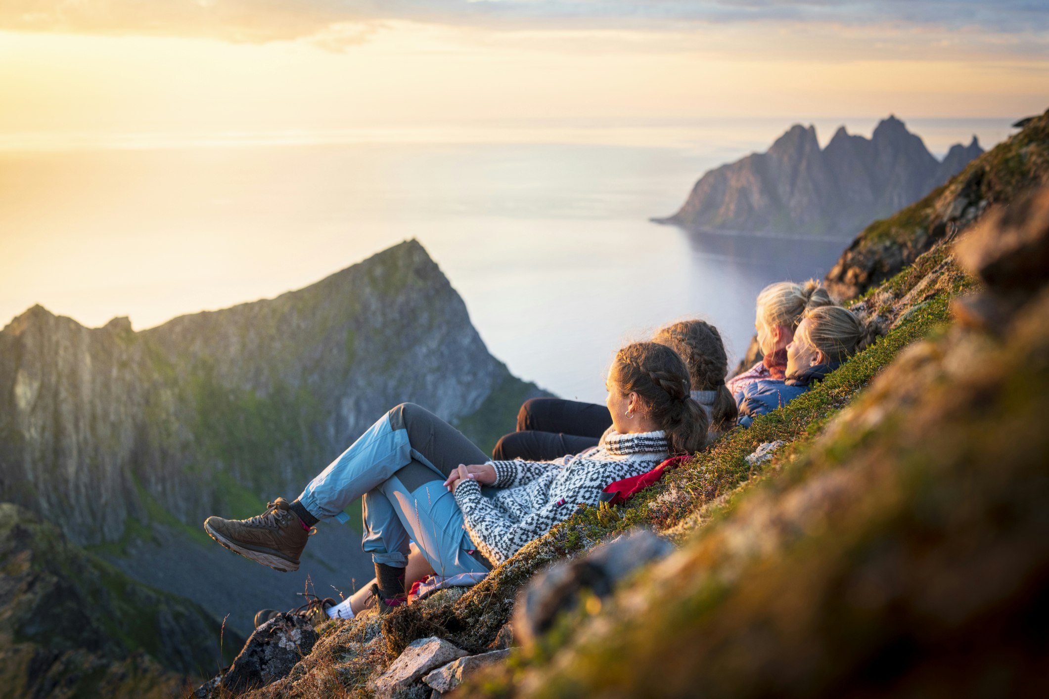Friends relaxing together at sunset lying down on mountain ridge, Senja island, Troms county, Norway